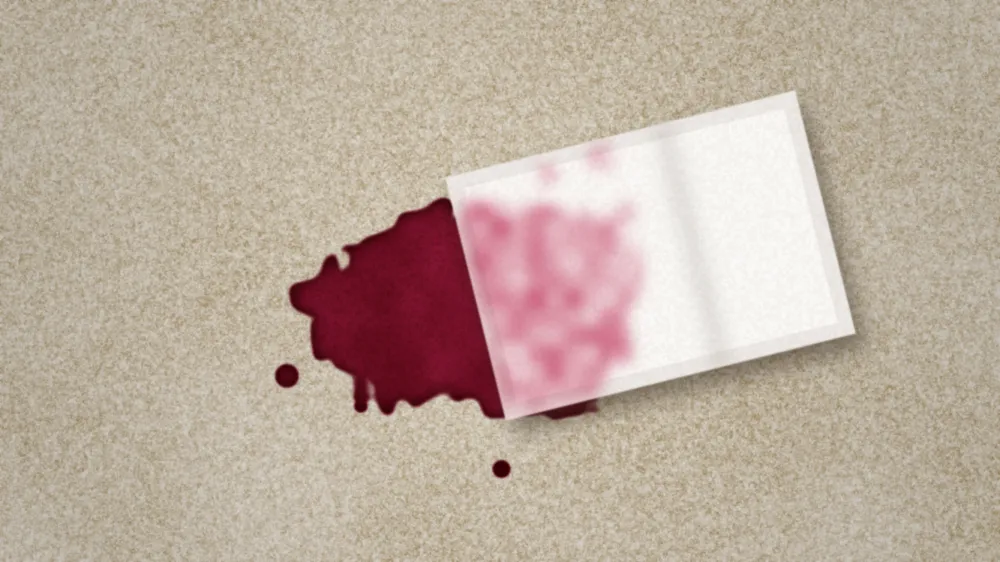 White towel blotting a fresh red wine spill on beige carpet